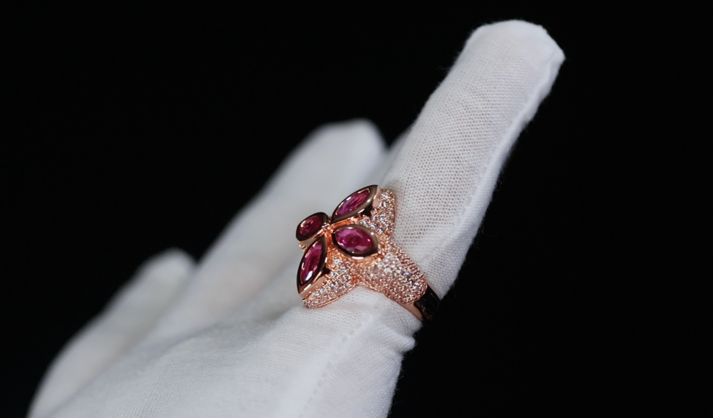 Ring with maroon gemstones on a white glove against a black background